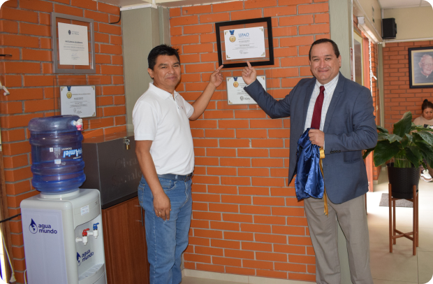 Dos exalumnos señalando un diploma en la pared del colegio